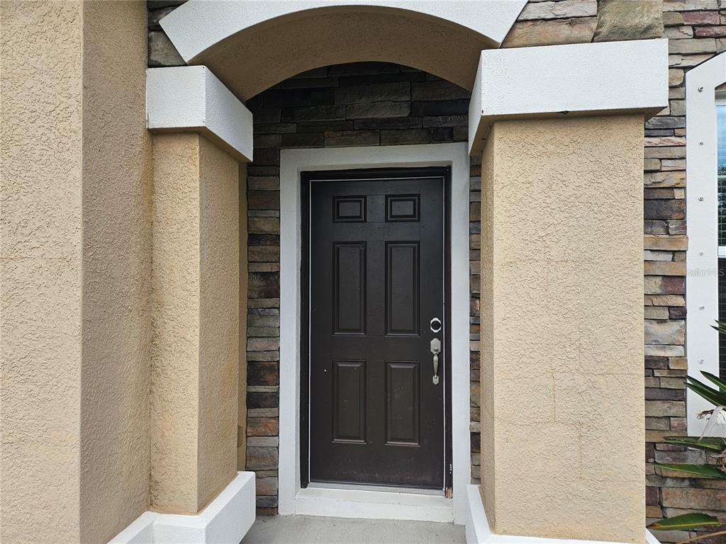 A dark brown front door is framed by stone veneer and beige stucco columns — 924 BUTTERCUP GLEN, BRADENTON, FL