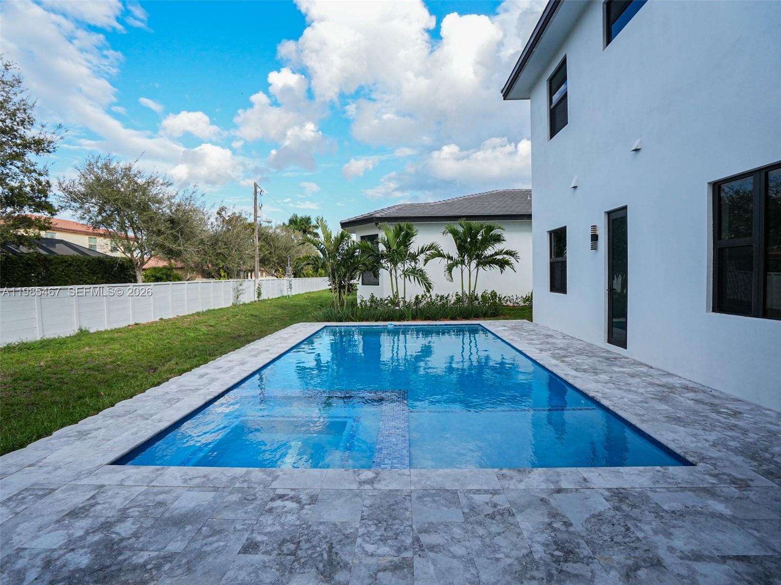 A rectangular swimming pool with a built-in spa sits beside a modern white house — 13004 Davie Oaks Dr, Davie FL 33325, DAVIE, FL