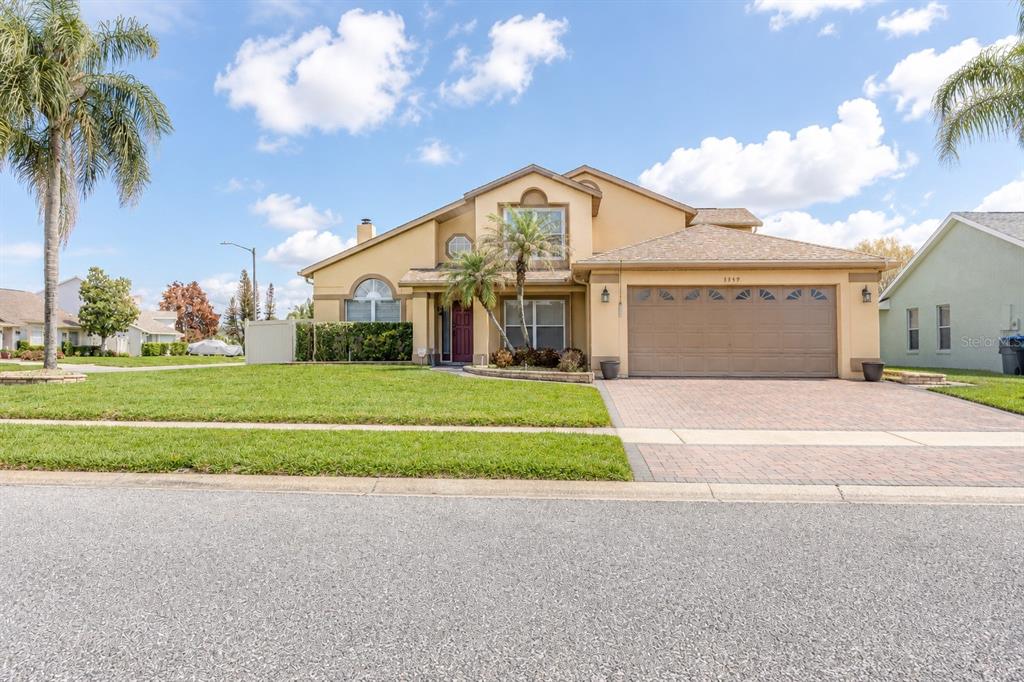 A two-story suburban house with a tan stucco exterior, a brick driveway, and palm trees — 3849 OCITA DRIVE, ORLANDO, FL