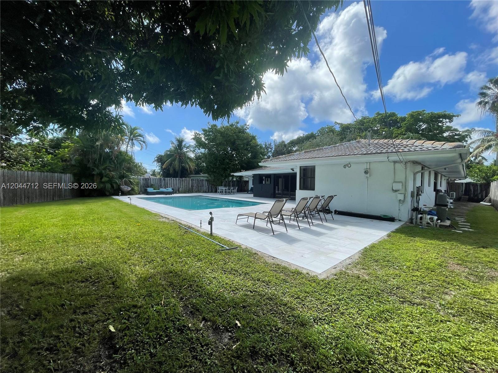 A backyard features a swimming pool, a paved patio with lounge chairs, and a white house — 2115 Alamanda Dr, North Miami FL 33181, NORTH MIAMI, FL