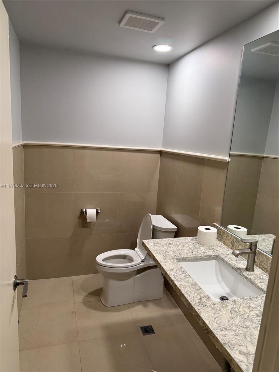 This bathroom features a toilet, a vanity with a stone countertop, and beige wall tiles — 219 N 21st Ave, Hollywood FL 33020, HOLLYWOOD, FL