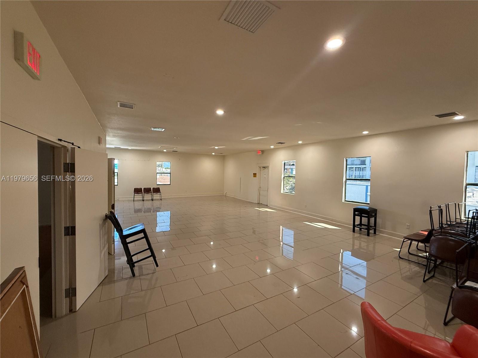 A large, empty room features light-colored tile flooring, white walls, and several windows — 219 N 21st Ave, Hollywood FL 33020, HOLLYWOOD, FL