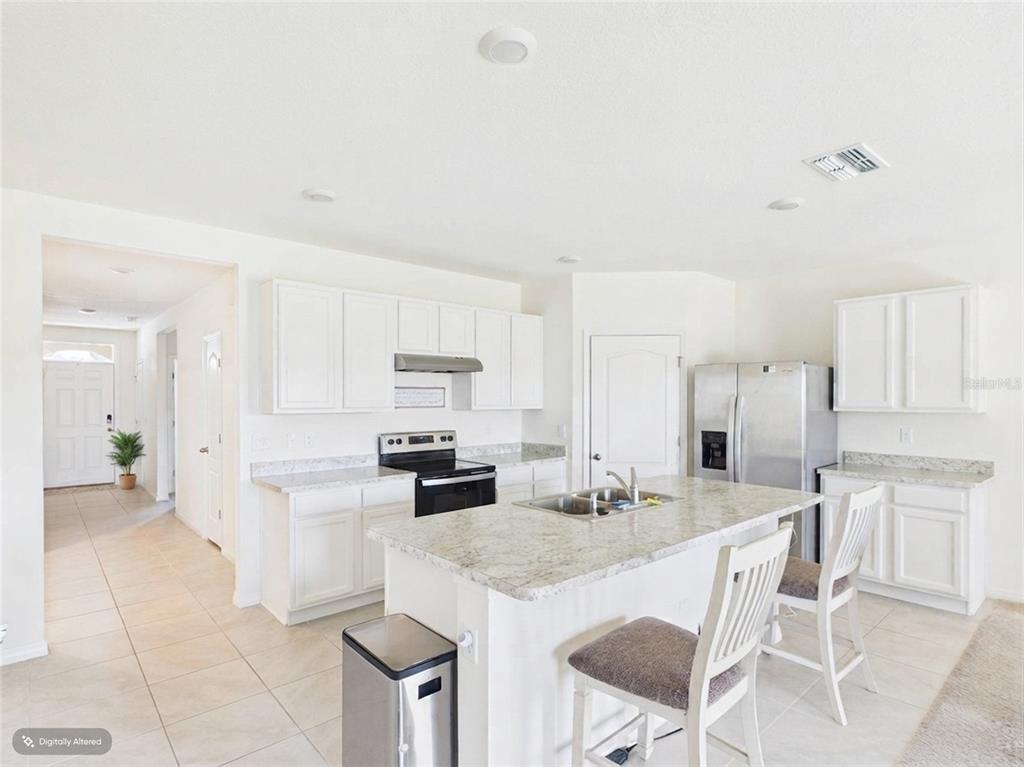 A bright kitchen features white cabinets, granite countertops, a center island, and stainless steel appliances — 804 AUBURN GROVE COURT, AUBURNDALE, FL