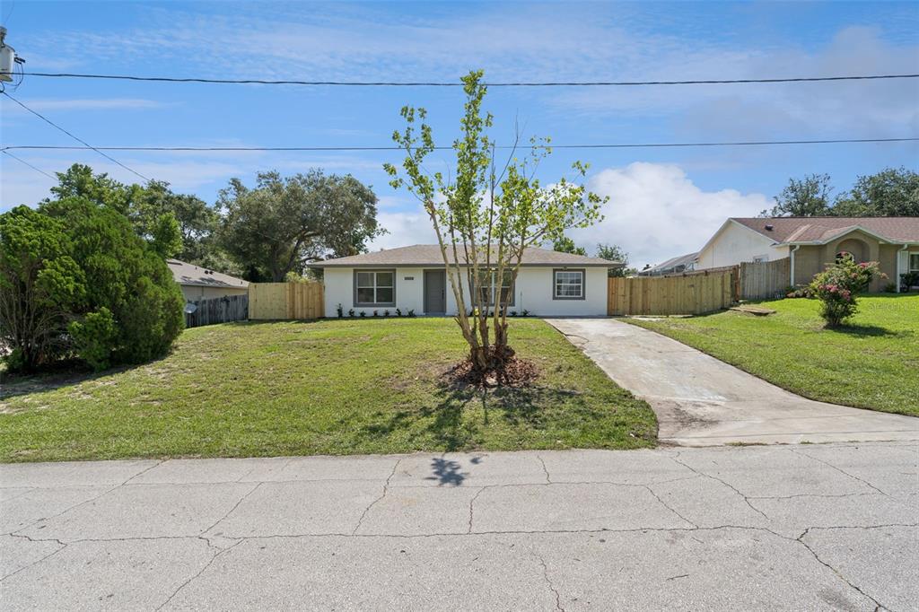A single-story house with a light-colored exterior, a concrete driveway, and a wooden fence — 2715 TIMBERLAKE AVENUE, DELTONA, FL