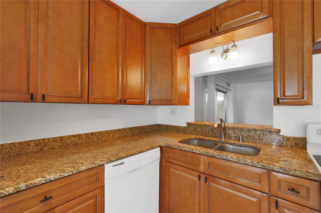 A kitchen with wood cabinets, granite countertops, a stainless steel sink, and a white dishwasher — 509 POLARIS LOOP UNIT 101, CASSELBERRY, FL
