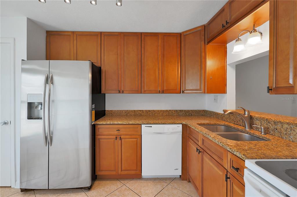 A kitchen features wood cabinets, granite countertops, a stainless steel refrigerator, and a white dishwasher — 509 POLARIS LOOP UNIT 101, CASSELBERRY, FL