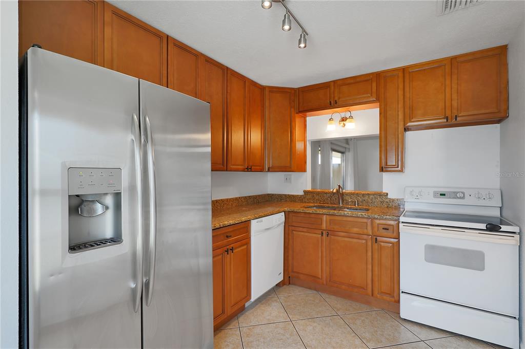 A kitchen features wood cabinets, granite countertops, a stainless steel refrigerator, and white appliances — 509 POLARIS LOOP UNIT 101, CASSELBERRY, FL