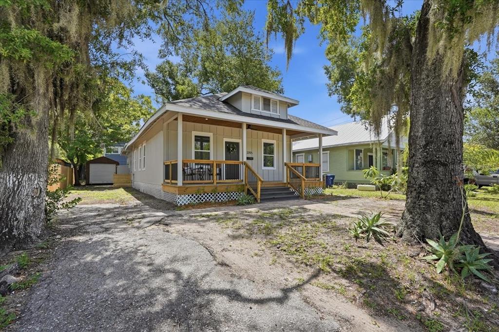 A single-story house with a front porch and wooden railings sits under large oak trees — 3705 N HIGHLAND AVENUE, TAMPA, FL