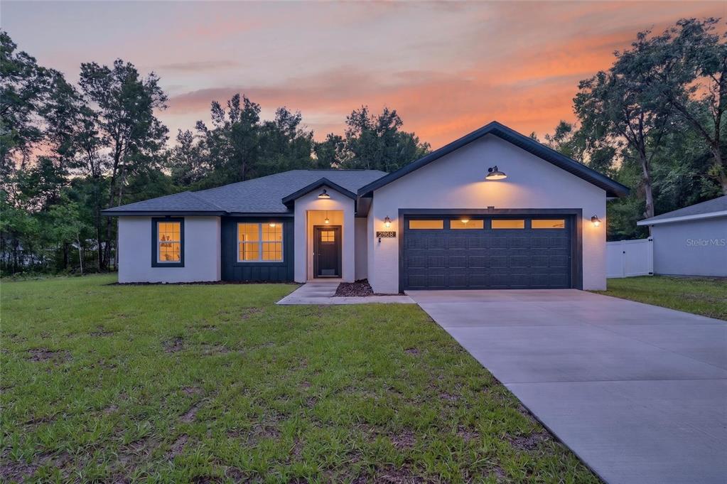 A modern single-story house with a two-car garage and a concrete driveway at sunset — 2968 SE 146 LANE, SUMMERFIELD, FL