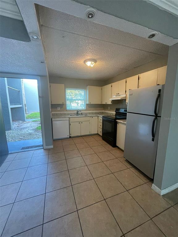 A kitchen with white cabinets, tile flooring, and a stainless steel refrigerator leads outside — 14413 AMERICANA CIRCLE UNIT 105, TAMPA, FL