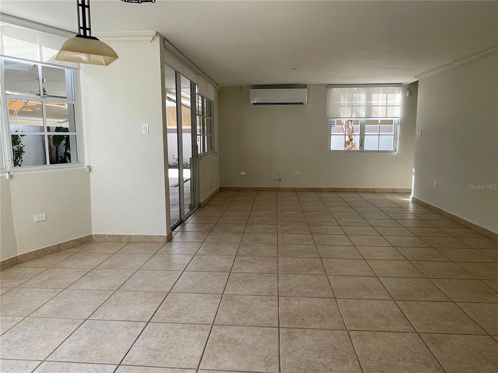 An empty room features beige tile flooring, white walls, a mini-split air conditioner, and windows — Palma Real COCO PLUMOSA, GUAYNABO, PR