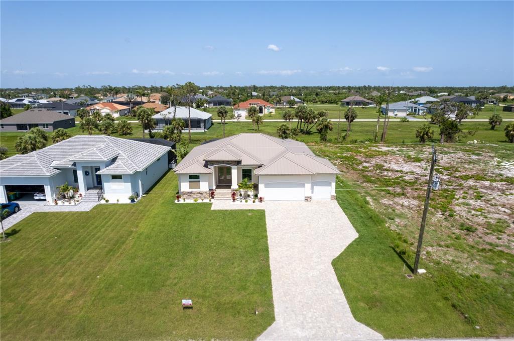 An aerial view shows a single-story house with a metal roof and paved driveway — 235 ROTONDA BOULEVARD S, ROTONDA WEST, FL