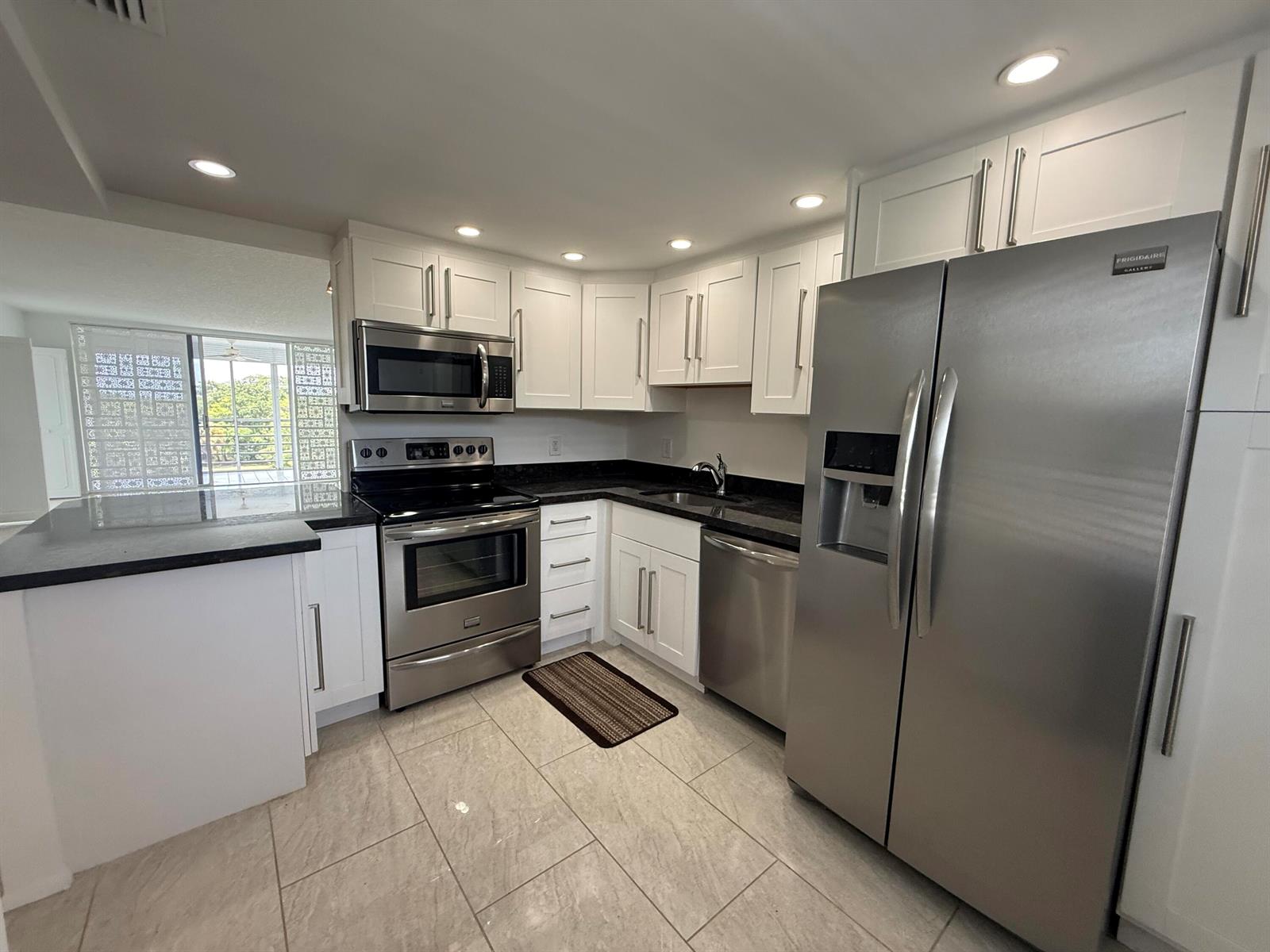 A kitchen with white cabinets, stainless steel appliances, and dark countertops on a tiled floor — 605 Oaks Drive # 602, Pompano Beach FL 33069, POMPANO BEACH, FL