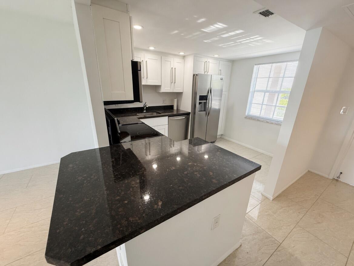A kitchen features white cabinets, dark granite countertops, stainless steel appliances, and light tile flooring — 605 Oaks Drive # 602, Pompano Beach FL 33069, POMPANO BEACH, FL