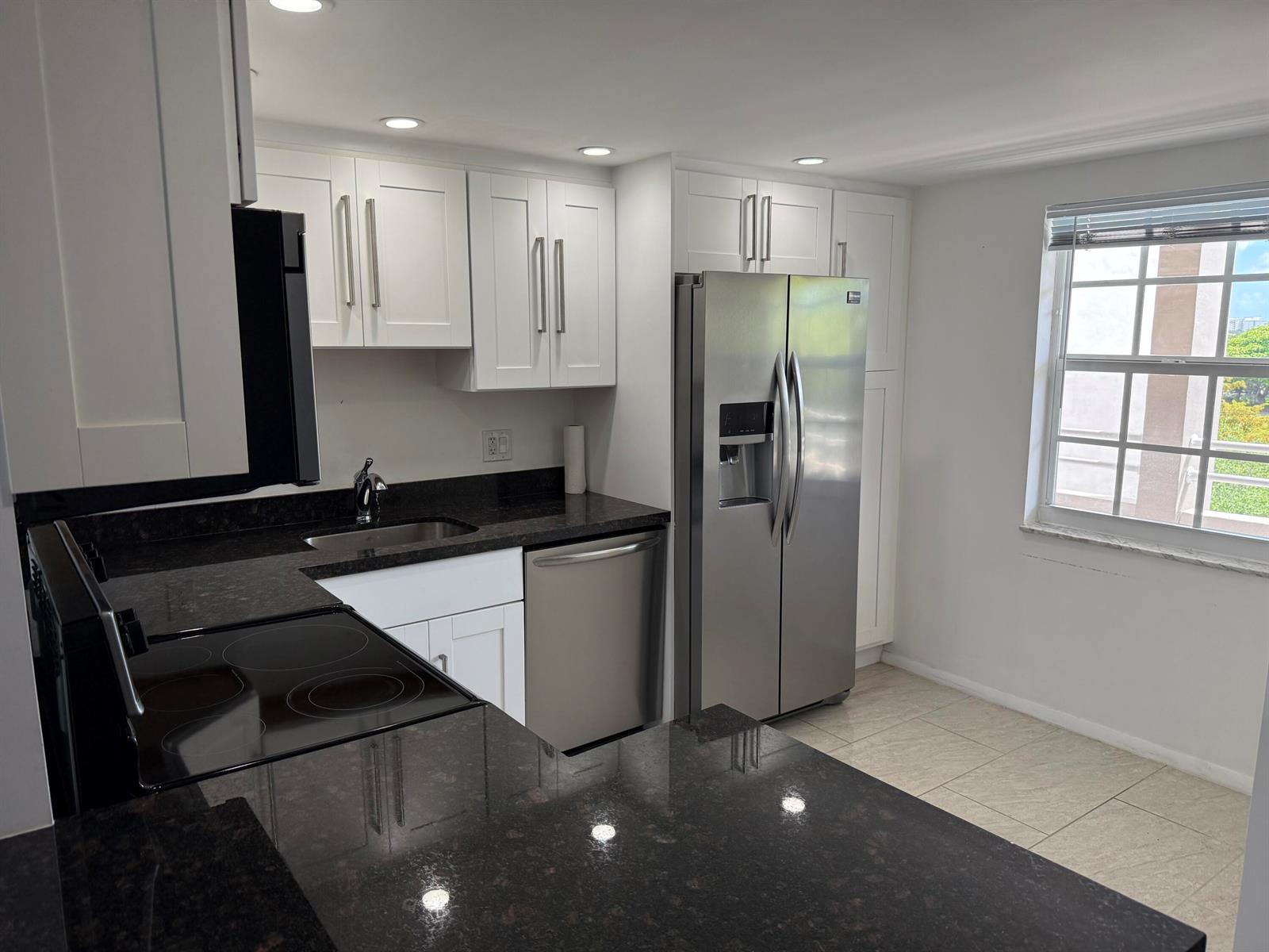 A kitchen features white cabinets, dark granite countertops, stainless steel appliances, and a window — 605 Oaks Drive # 602, Pompano Beach FL 33069, POMPANO BEACH, FL