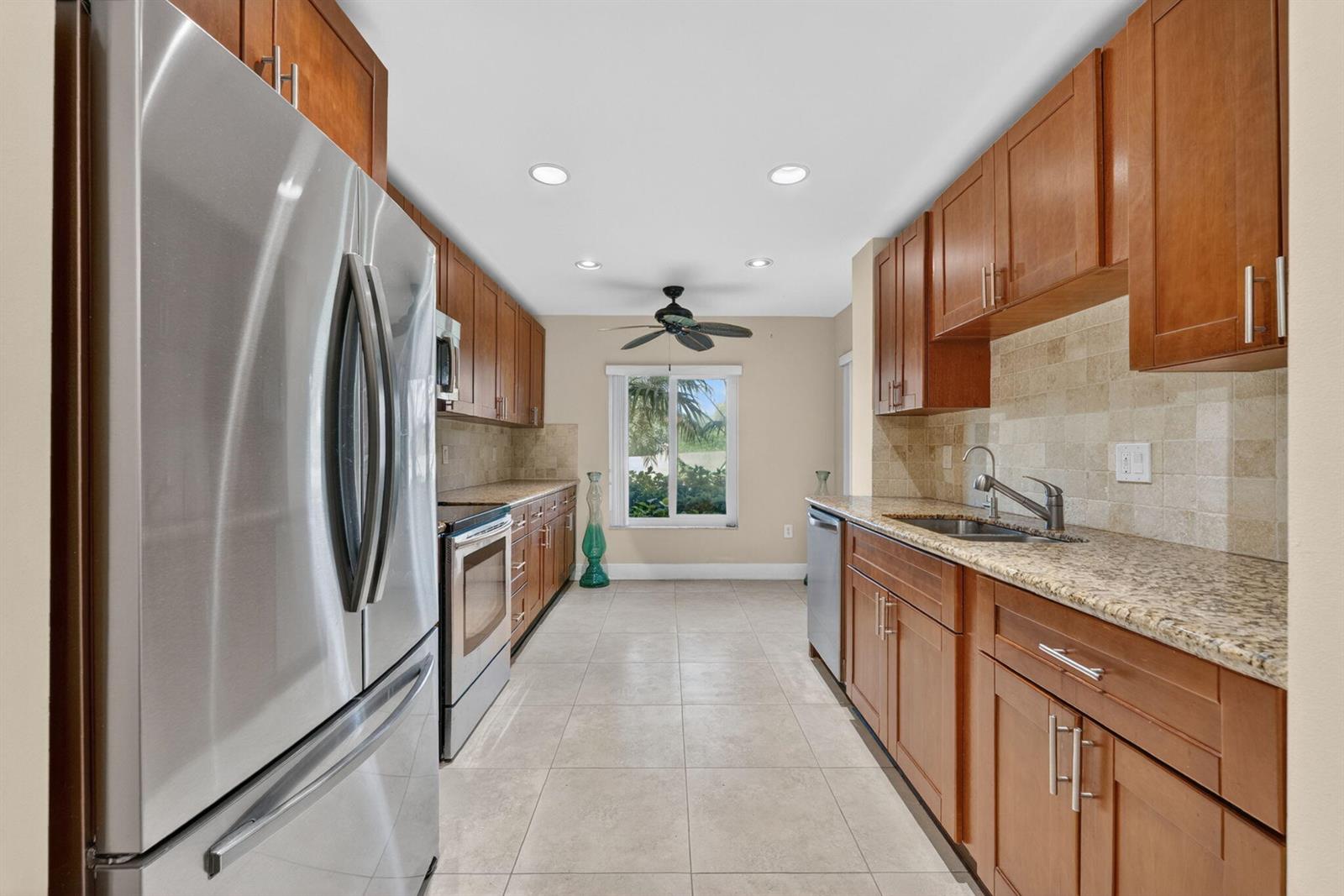 A galley kitchen features wood cabinets, granite countertops, stainless steel appliances, and tile flooring — 16353 Malibu Drive # 61, Weston FL 33326, WESTON, FL