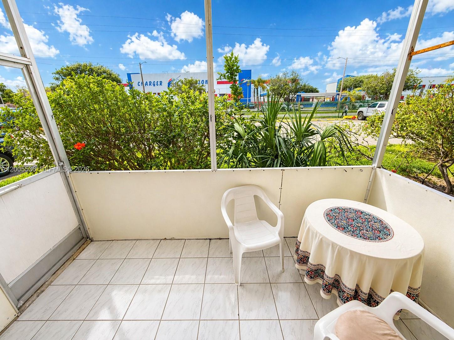 A screened-in patio features white tiled flooring, a small round table, and two plastic chairs — 16701 NE 13th Ave # 102, Miami FL 33162, MIAMI, FL