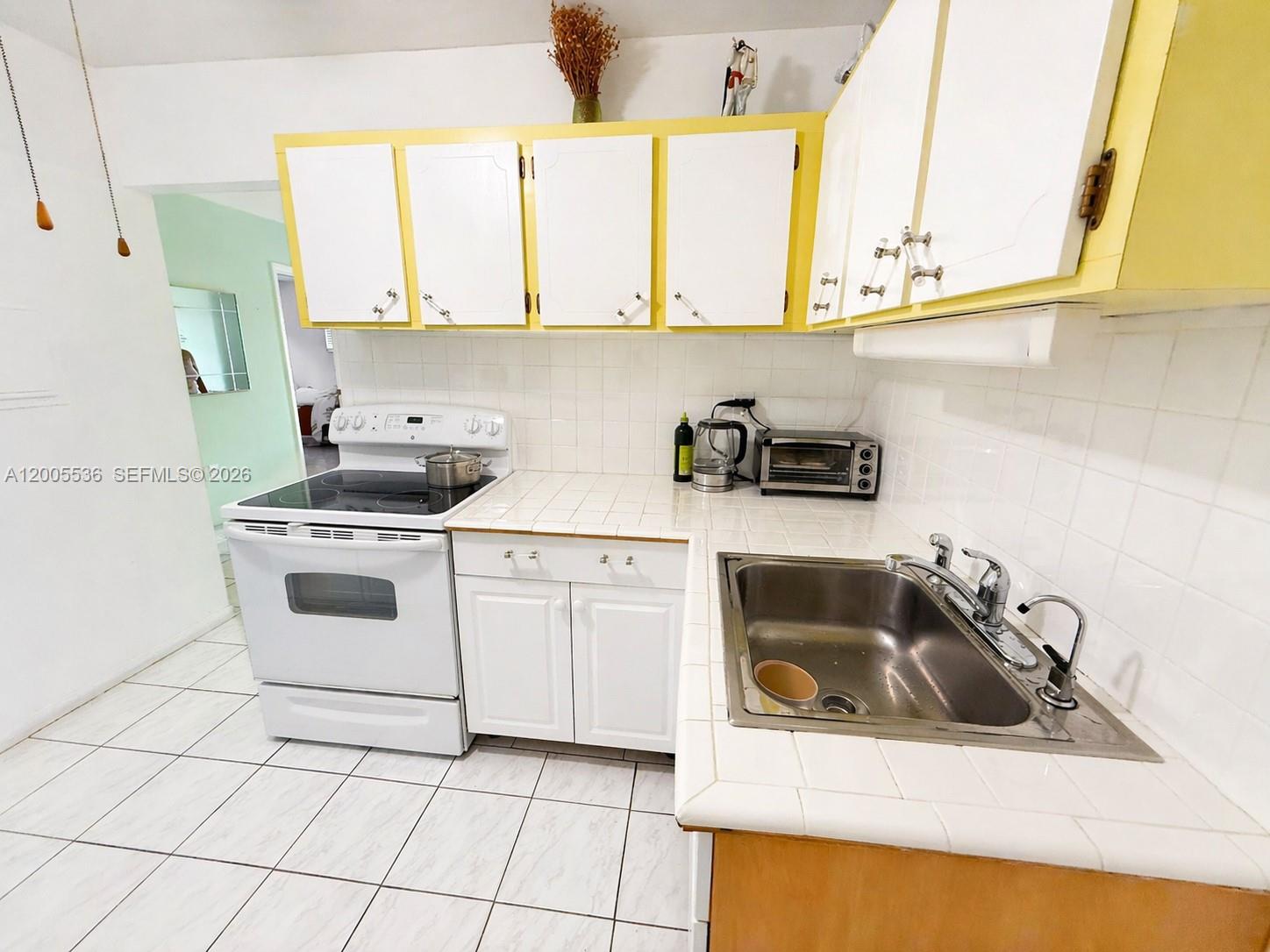 A kitchen features white cabinets with yellow trim, white tiled countertops, and white appliances — 16701 NE 13th Ave # 102, Miami FL 33162, MIAMI, FL
