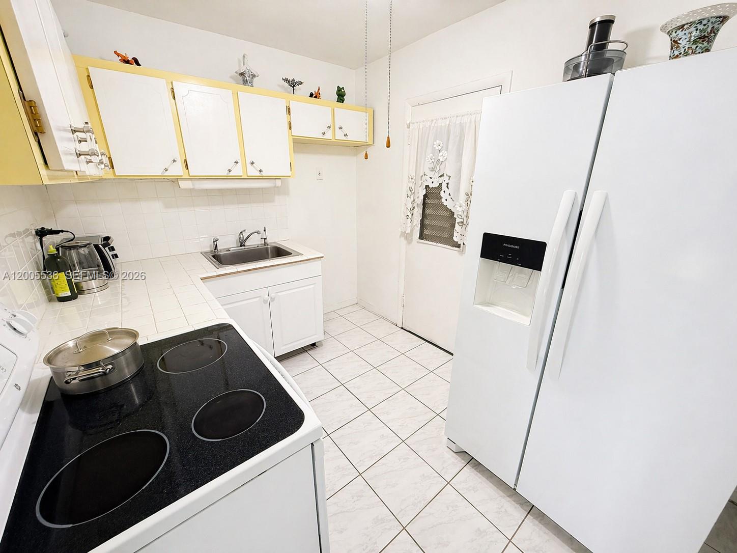 A kitchen features white cabinets with yellow trim, a black electric stove, and white appliances — 16701 NE 13th Ave # 102, Miami FL 33162, MIAMI, FL