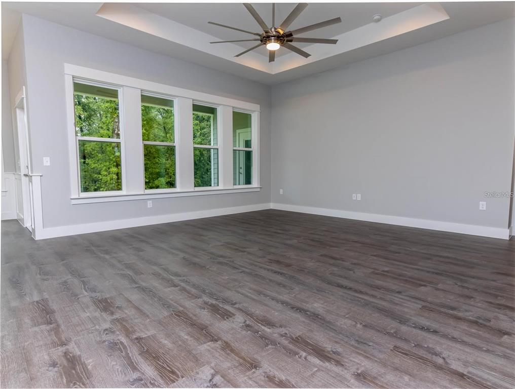 An empty room features gray walls, wood-look flooring, a tray ceiling, and large windows — 137 SW CADENCE GLEN, LAKE CITY, FL
