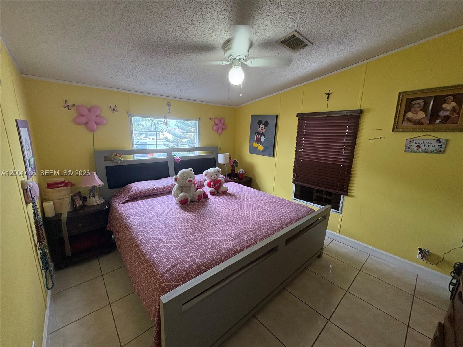 A bedroom with yellow walls, tile flooring, a ceiling fan, and a gray bed frame — 1110 SW 131 PL, Miami FL 33184, MIAMI, FL