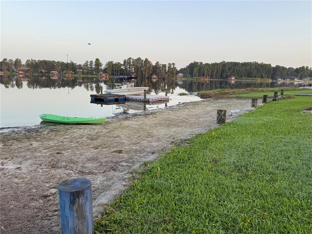 A green kayak sits on a sandy lakeshore near a boat docked at a pier — 3545 LAKE PADGETT DRIVE, LAND O LAKES, FL