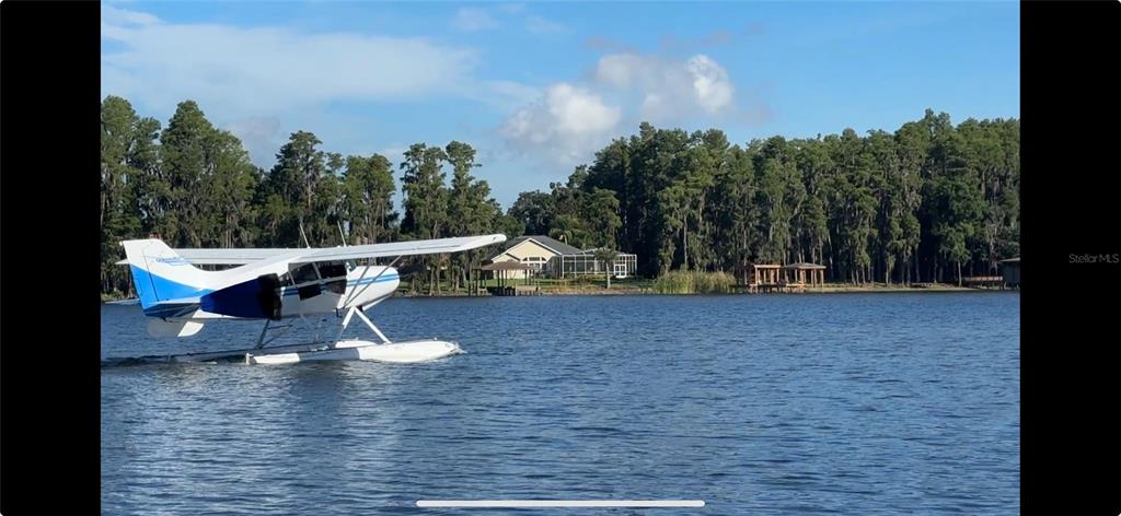 A seaplane floats on a lake in front of a house and wooded shoreline — 3545 LAKE PADGETT DRIVE, LAND O LAKES, FL