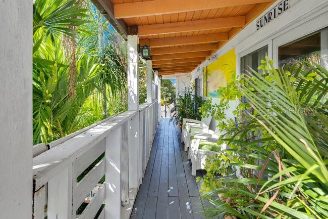 A wooden balcony with a white railing overlooks lush greenery and features outdoor seating — PELICAN ESTATE-PUNTAS- CARR 413 KM 3.3, RINCON, PR