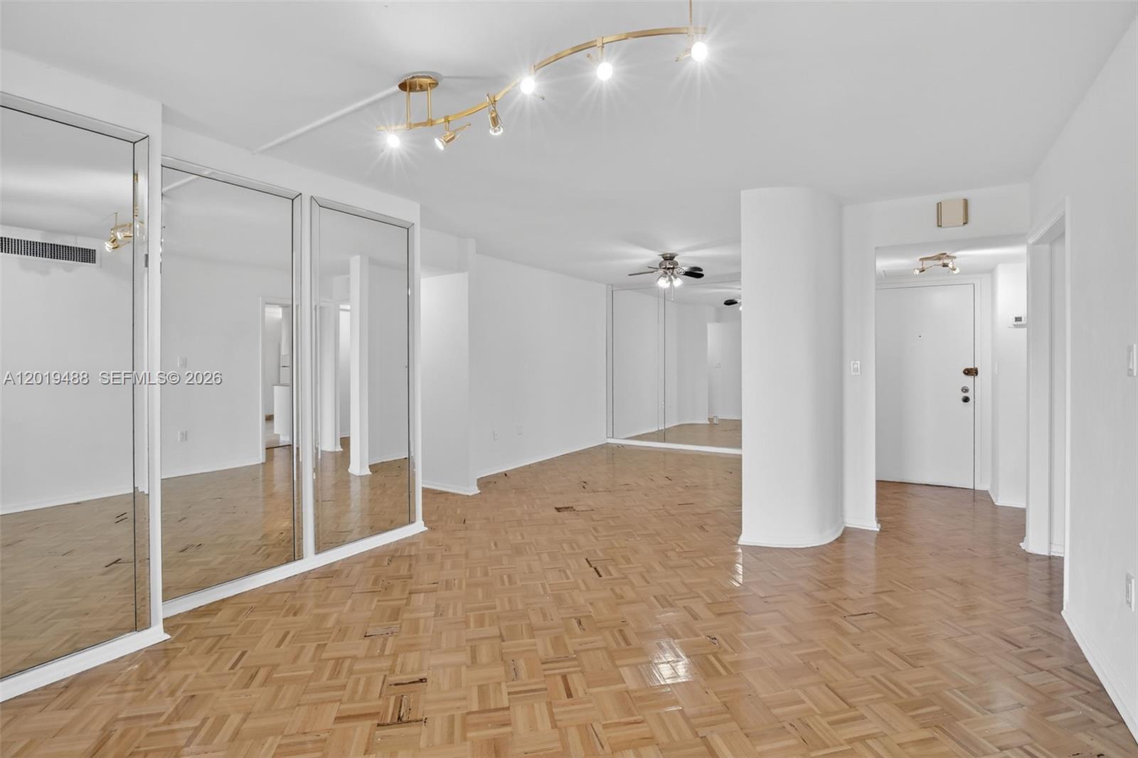 An empty room features parquet wood flooring, mirrored closet doors, and a curved structural column — 2808 N 46th Ave # E654, Hollywood FL 33021, HOLLYWOOD, FL