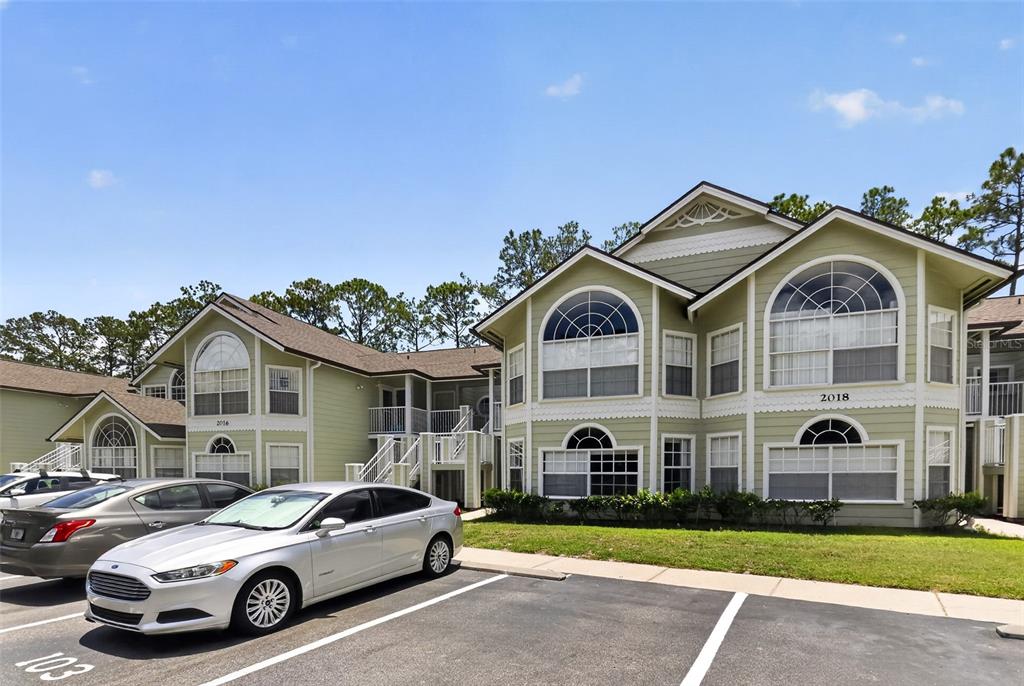 A two-story apartment building with light green siding and arched windows sits behind a parking lot — 2016 ROYAL BAY BOULEVARD UNIT 103, KISSIMMEE, FL