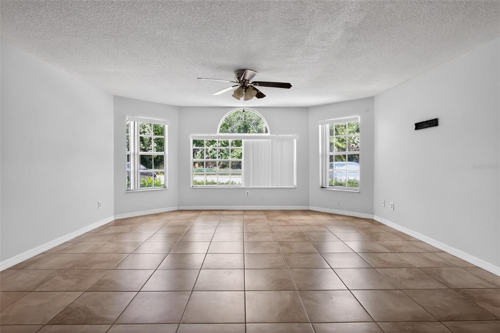 An empty living room features light-colored walls, large windows, a ceiling fan, and tiled floors — 2016 ROYAL BAY BOULEVARD UNIT 103, KISSIMMEE, FL