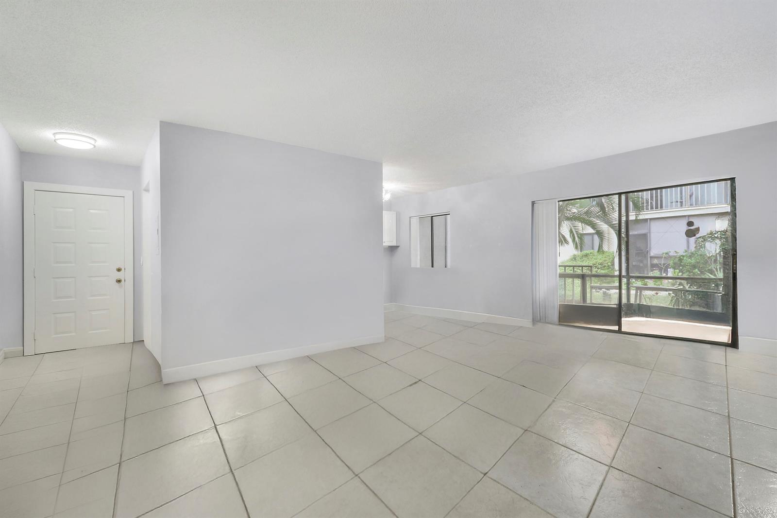 An empty living room with light-colored tile flooring, white walls, and a sliding glass door — 150 Pineview Road # C4, Jupiter FL 33469, JUPITER, FL