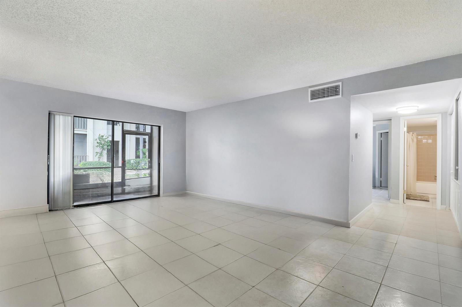 An empty living room with light-colored tile flooring, gray walls, and a sliding glass door — 150 Pineview Road # C4, Jupiter FL 33469, JUPITER, FL