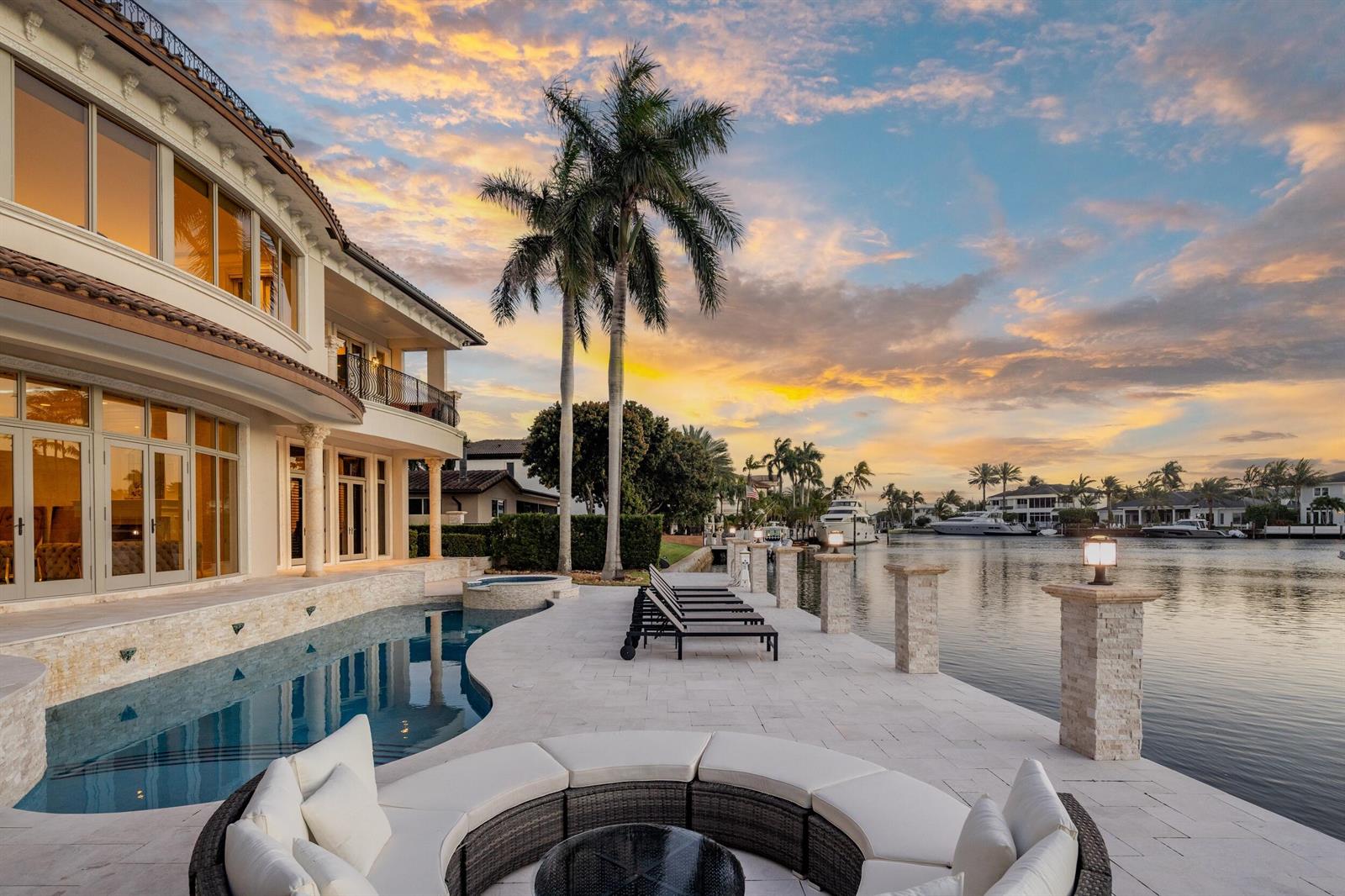 A luxury waterfront home features a curved pool, patio seating, and palm trees at sunset — 3201 NE 27th Avenue, Lighthouse Point FL 33064, LIGHTHOUSE POINT, FL