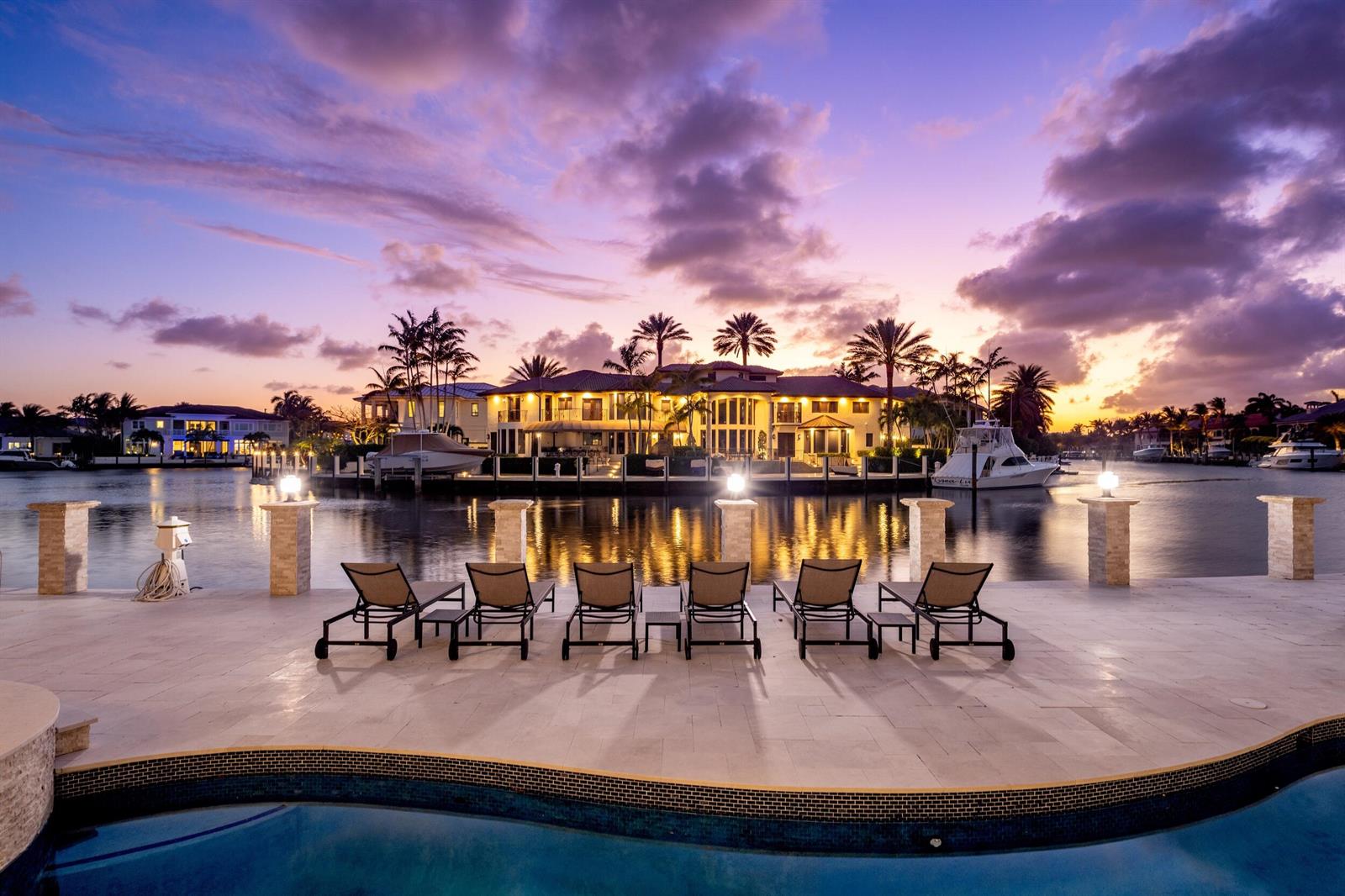 A waterfront patio features six lounge chairs overlooking a canal and a large luxury home — 3201 NE 27th Avenue, Lighthouse Point FL 33064, LIGHTHOUSE POINT, FL