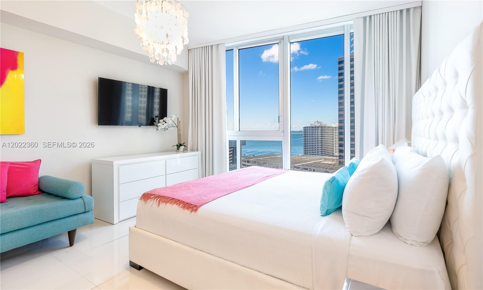 A modern bedroom features a white tufted headboard, a blue sofa, and floor-to-ceiling windows — MIAMI, FL