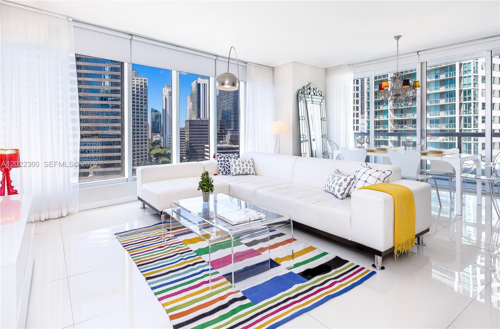 A modern living room features a white sectional sofa, glass coffee table, and colorful striped rug — MIAMI, FL