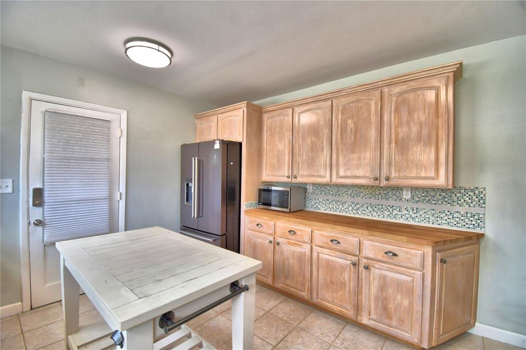A kitchen features light wood cabinets, a wooden countertop, a mosaic backsplash, and a white island — 1620 17TH STREET NW, WINTER HAVEN, FL