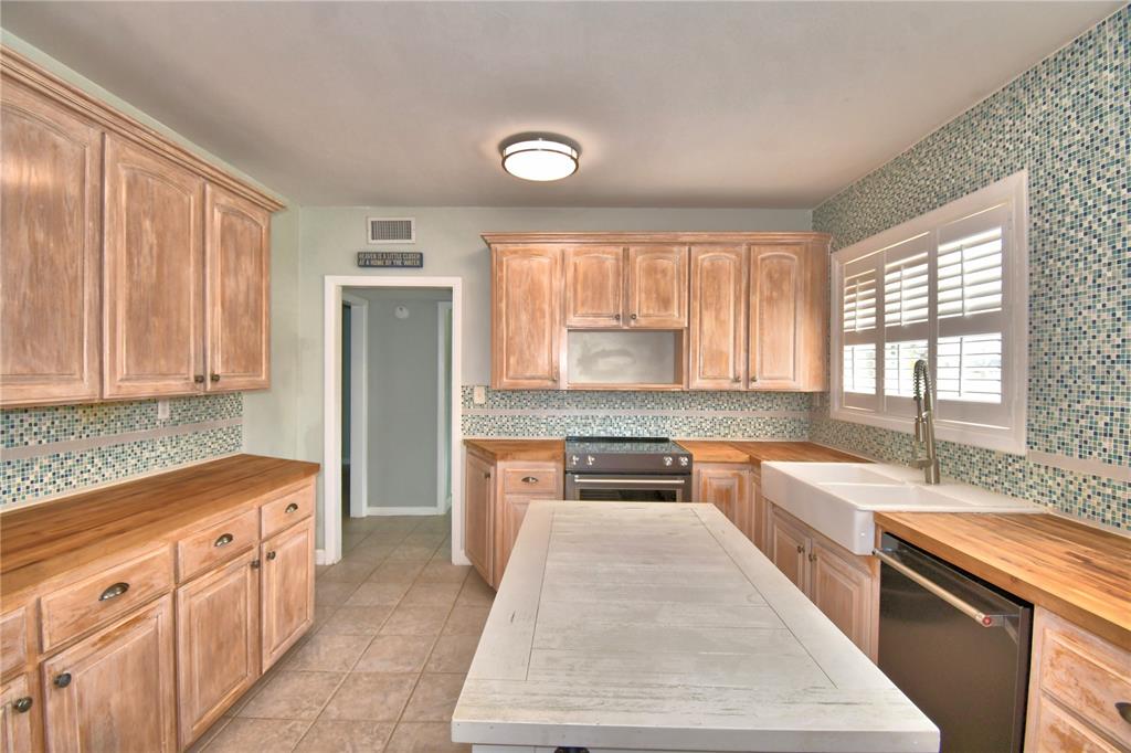 A kitchen with light wood cabinets, butcher block countertops, a white island, and mosaic tile — 1620 17TH STREET NW, WINTER HAVEN, FL