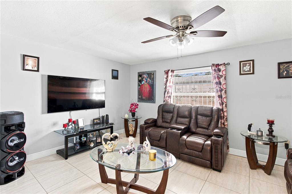 A living room features a wall-mounted television, a brown leather loveseat, and a glass coffee table — 6513 N MANHATTAN AVENUE, TAMPA, FL