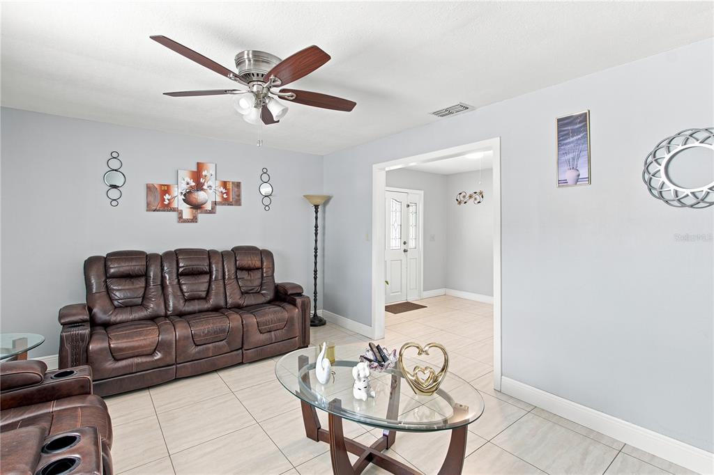A living room features a brown leather sofa, a glass coffee table, and tile flooring — 6513 N MANHATTAN AVENUE, TAMPA, FL