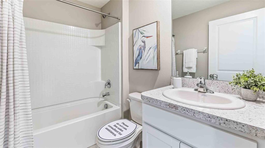 A bathroom features a white vanity with a speckled countertop, a toilet, and a tub-shower — 35489 SUNFLOWER HILL DRIVE, ZEPHYRHILLS, FL
