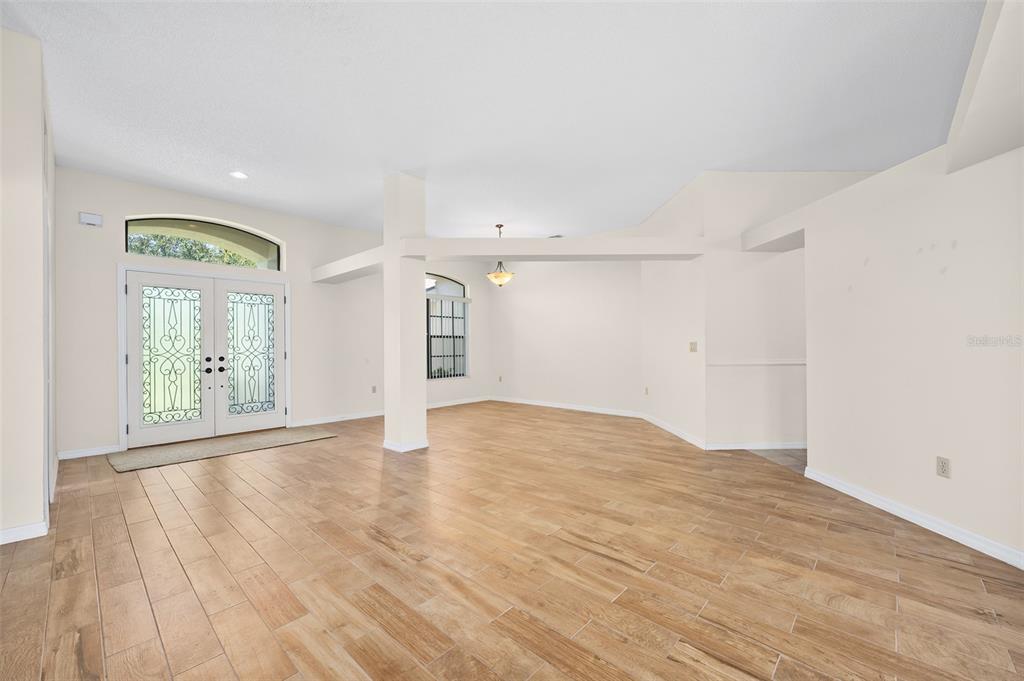 An open-concept living area features light wood-look tile flooring and a white double-door entrance — 1837 E GLANCY DRIVE, DELTONA, FL