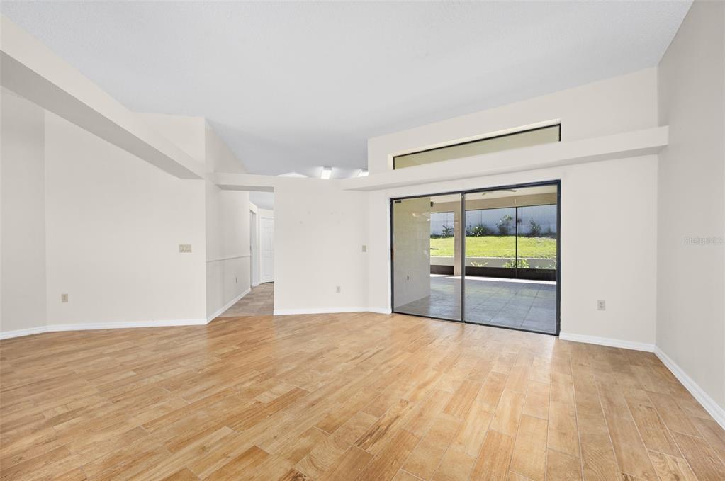 An empty living room features light wood-look tile flooring, white walls, and sliding glass doors — 1837 E GLANCY DRIVE, DELTONA, FL