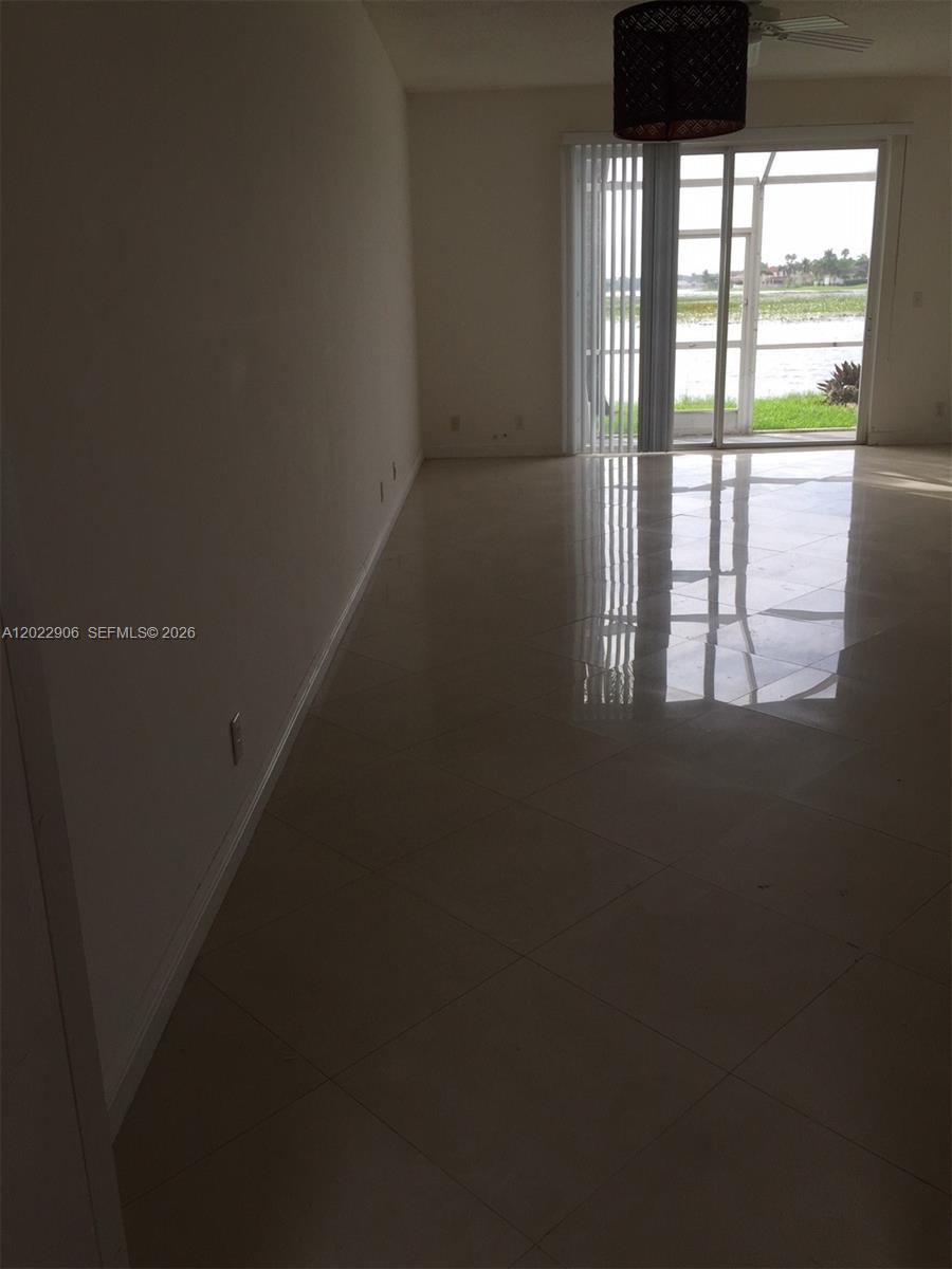 An empty room features light-colored tile flooring, a dark pendant light, and a sliding glass door — 1804 Salerno Cir # 1804, Weston FL 33327, WESTON, FL