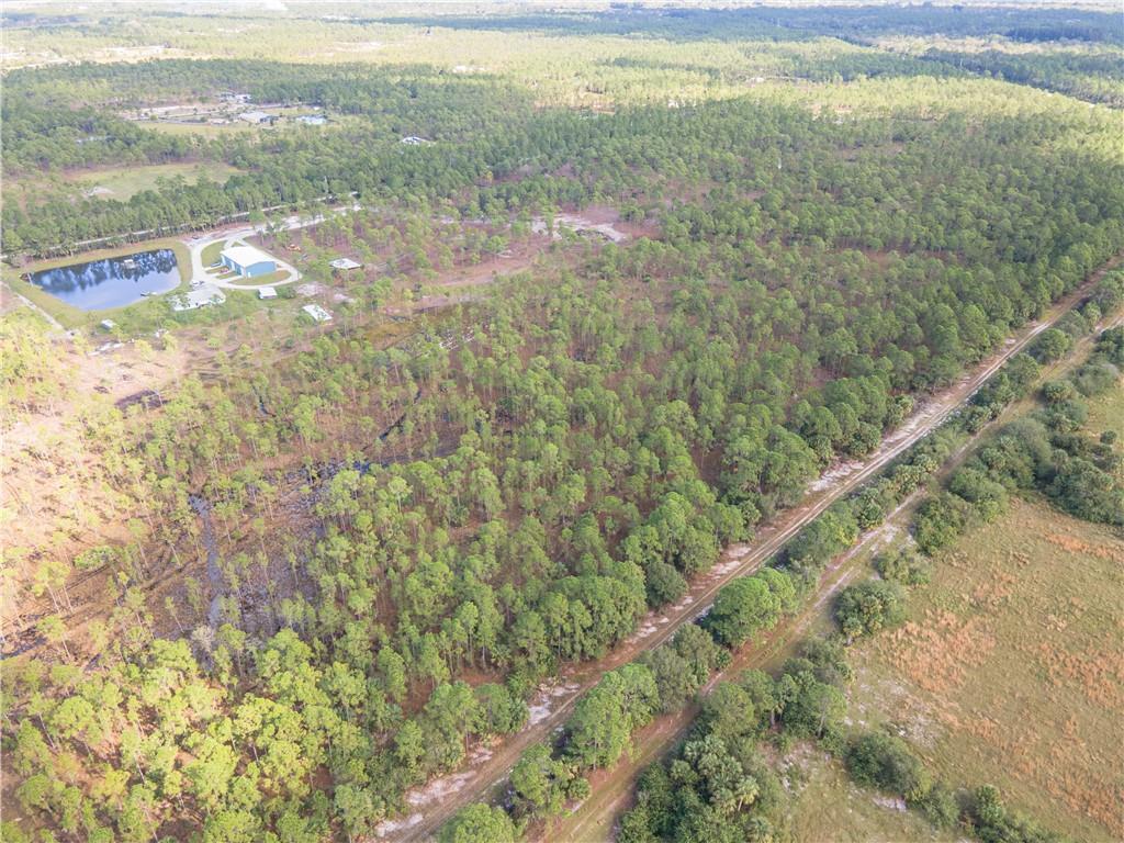 An aerial view shows a wooded lot with a pond and a dirt road — FELLSMERE, FL