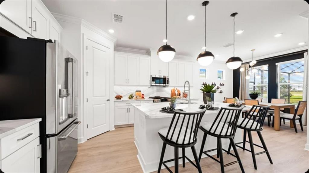 A modern white kitchen features a marble-topped island with black stools and pendant lighting — 7424 MOONBEAM AVENUE, SARASOTA, FL