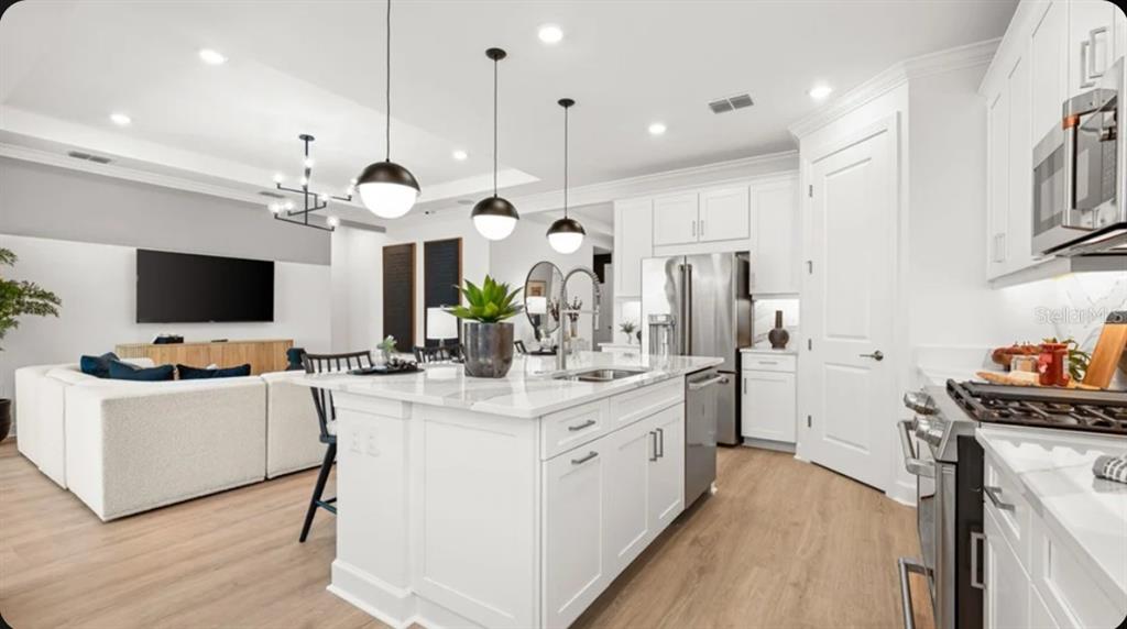 A modern open-concept kitchen features white cabinetry, a large marble-topped island, and light wood flooring — 7424 MOONBEAM AVENUE, SARASOTA, FL