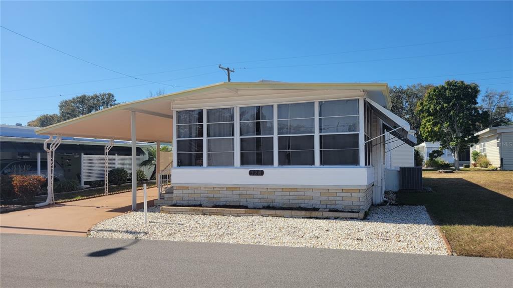 A single-story mobile home features a screened-in front porch, a carport, and stone-patterned skirting — 585 SKY HARBOR DRIVE UNIT 326, CLEARWATER, FL