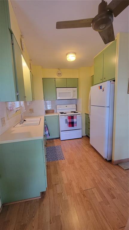 A galley kitchen features light green cabinets, white appliances, and wood-look flooring — 585 SKY HARBOR DRIVE UNIT 326, CLEARWATER, FL
